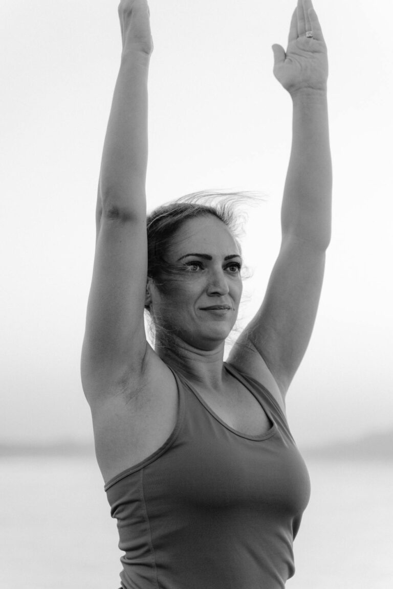 A woman practicing yoga outdoors with her arms raised, captured in black and white for a serene effect.